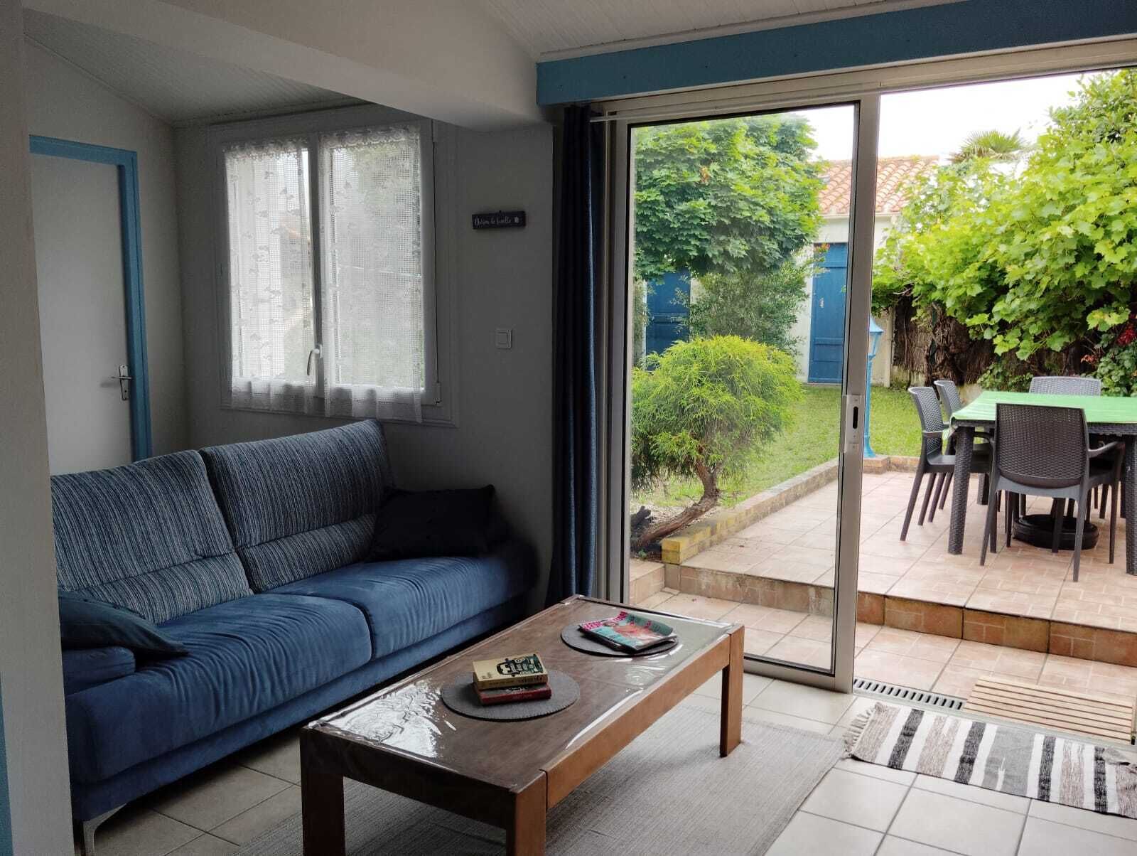 A living room with a blue sofa, a wooden coffee table, and a sliding glass door leading to an outdoor patio with a table and chairs.