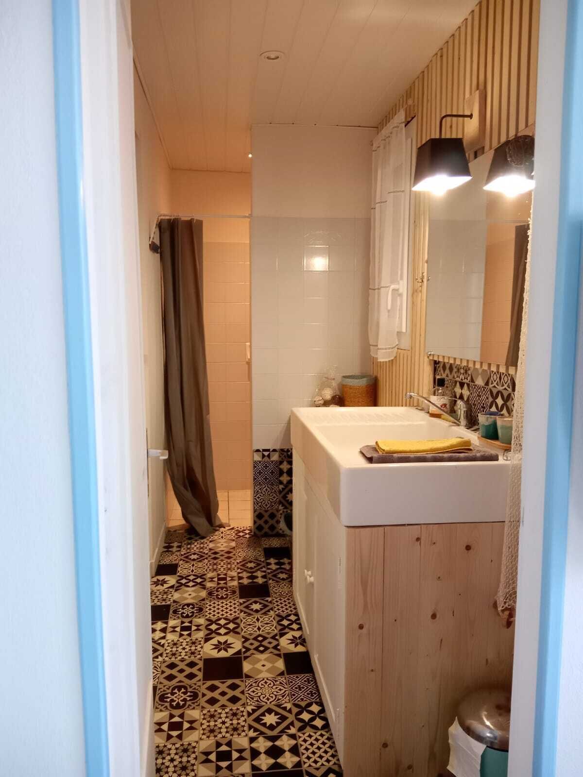 Ein Badezimmer mit einem gemusterten Boden, einem Waschbecken mit Spiegel und einer Duschvorhang.