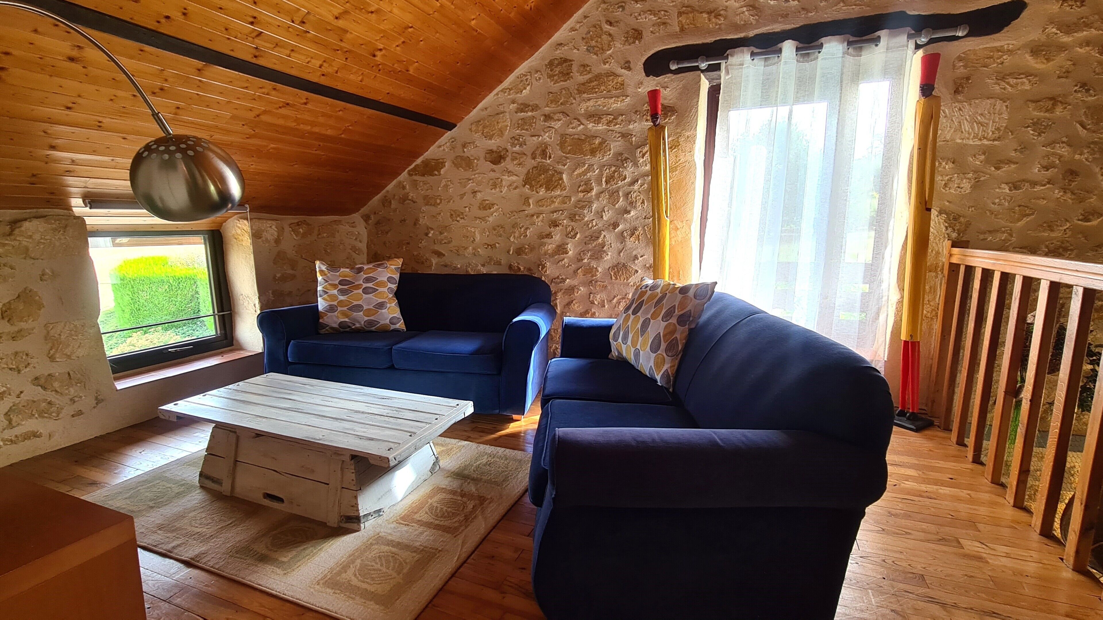 Ein gemütliches Zimmer mit Steinwand, einem blauen Sofa, einem Holztisch und einem fenster mit Vorhängen.