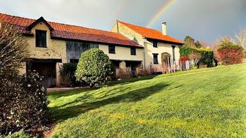 Een huis met een rood dak, een grote voortuin en een regenboog aan de lucht.