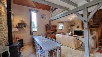 A rustic interior with a stone floor, wooden beams, a dining area with a table and chairs, a sofa, and a television.