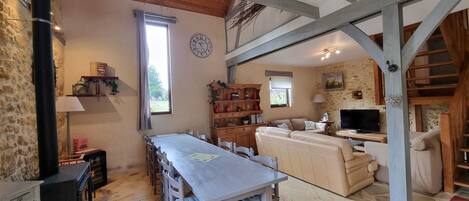 Un'atmosfera rustica con pavimento in pietra, travi in legno, zona pranzo con tavolo e sedie, un divano e un televisore.