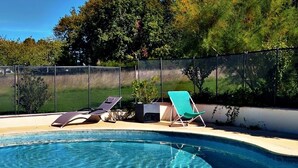 Una piscina con agua cristalina y azul, rodeada por una cerca y dos tumbonas.