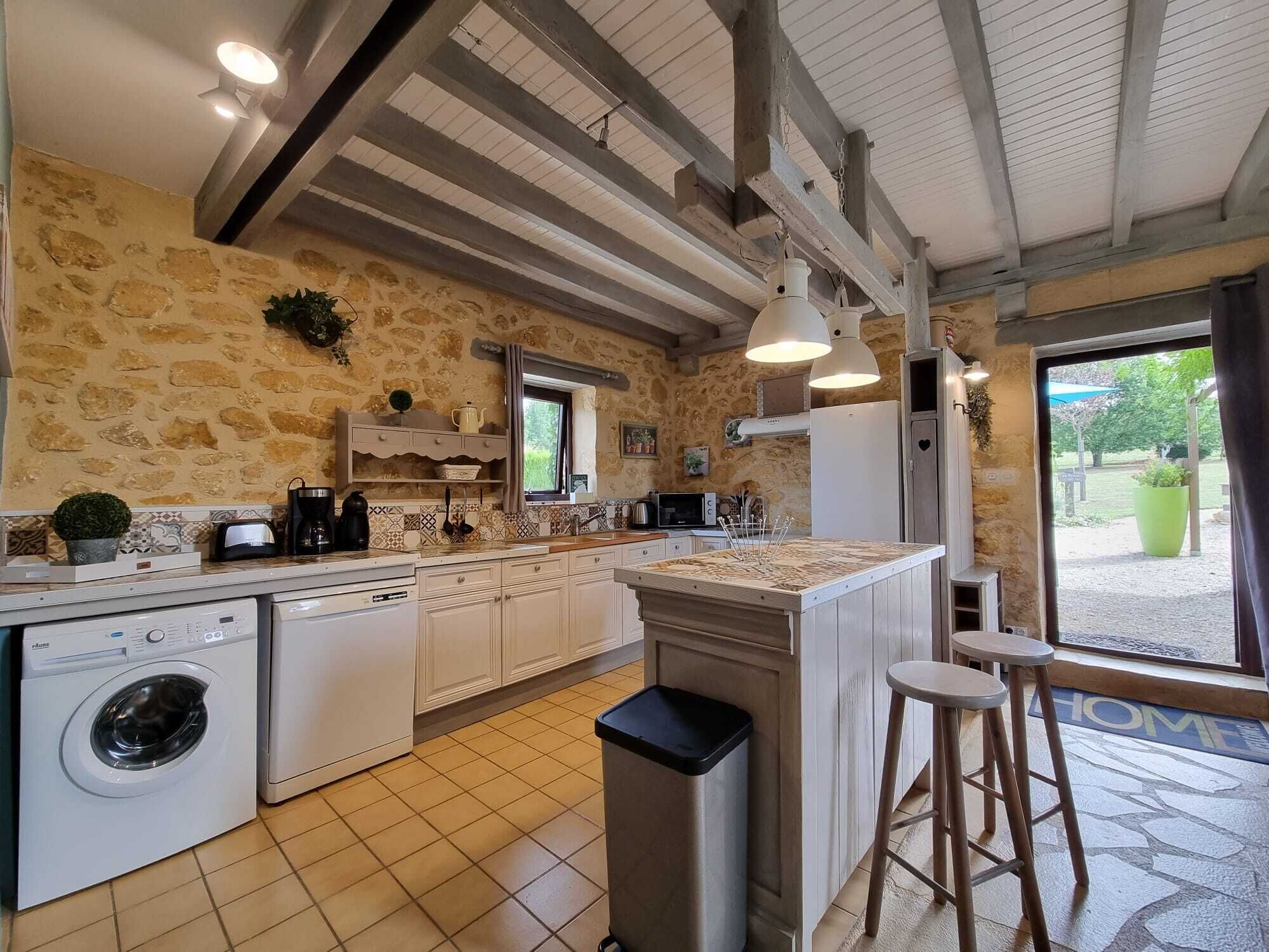 Cocina con paredes de piedra, lavadora, lavabo y ventana con vistas a un jardín.
