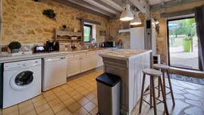 Cocina con paredes de piedra, lavadora, lavabo y ventana con vistas a un jardín.