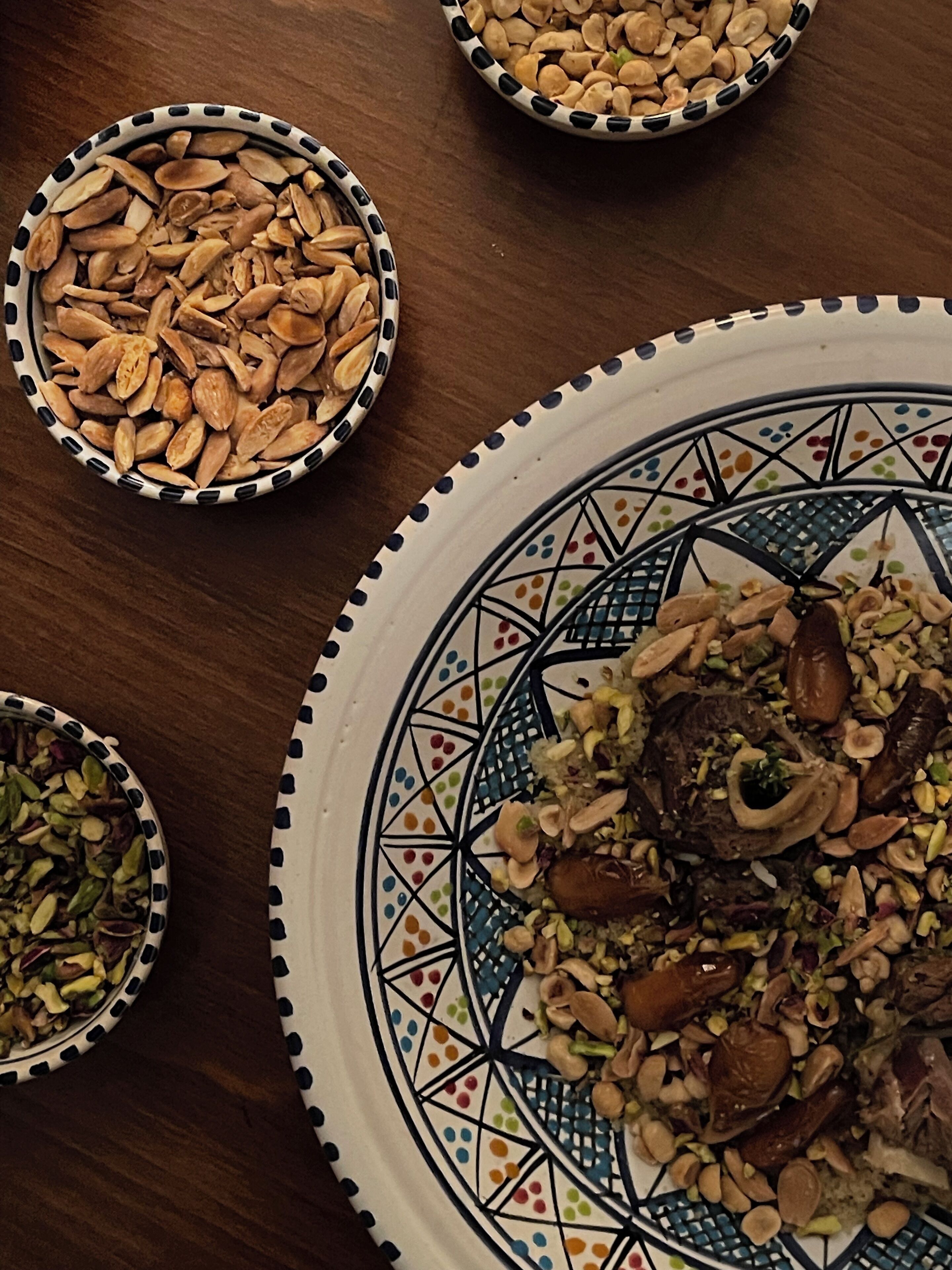 Una mesa con tres recipientes con frutos secos y frutas deshidratadas, y un plato decorativo con un diseño geométrico.