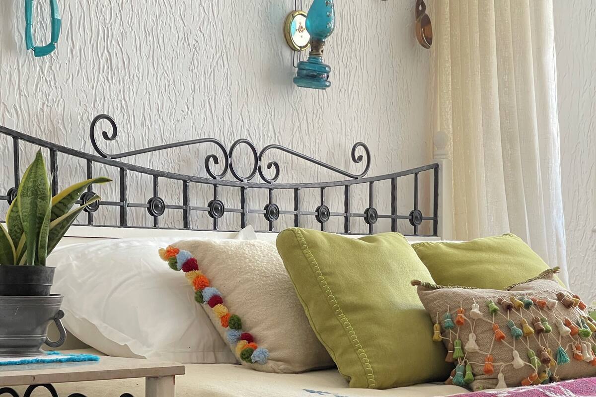 Una cama con cabecera de metal, una planta en maceta y almohadas coloridas.