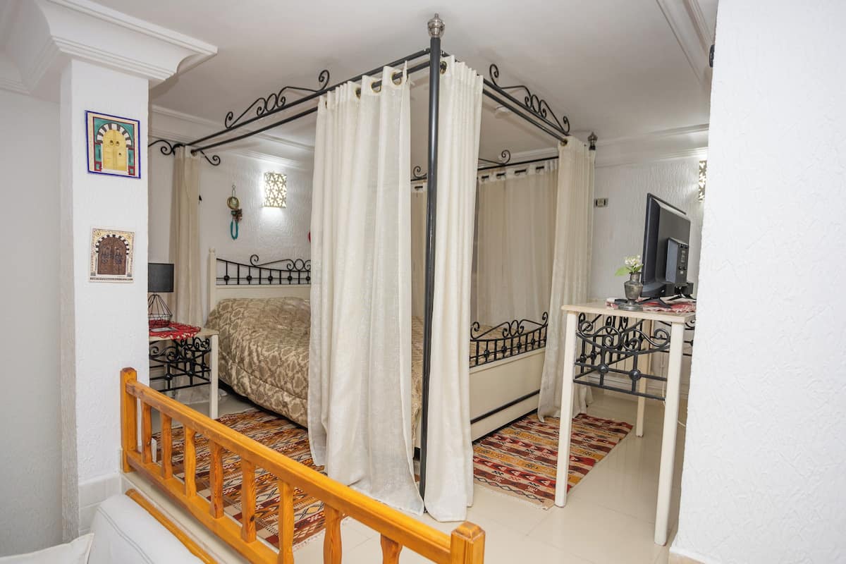Una cama con dosel y largueros, un tablero de noche con lámpara y un televisor sobre un mueble bajo.