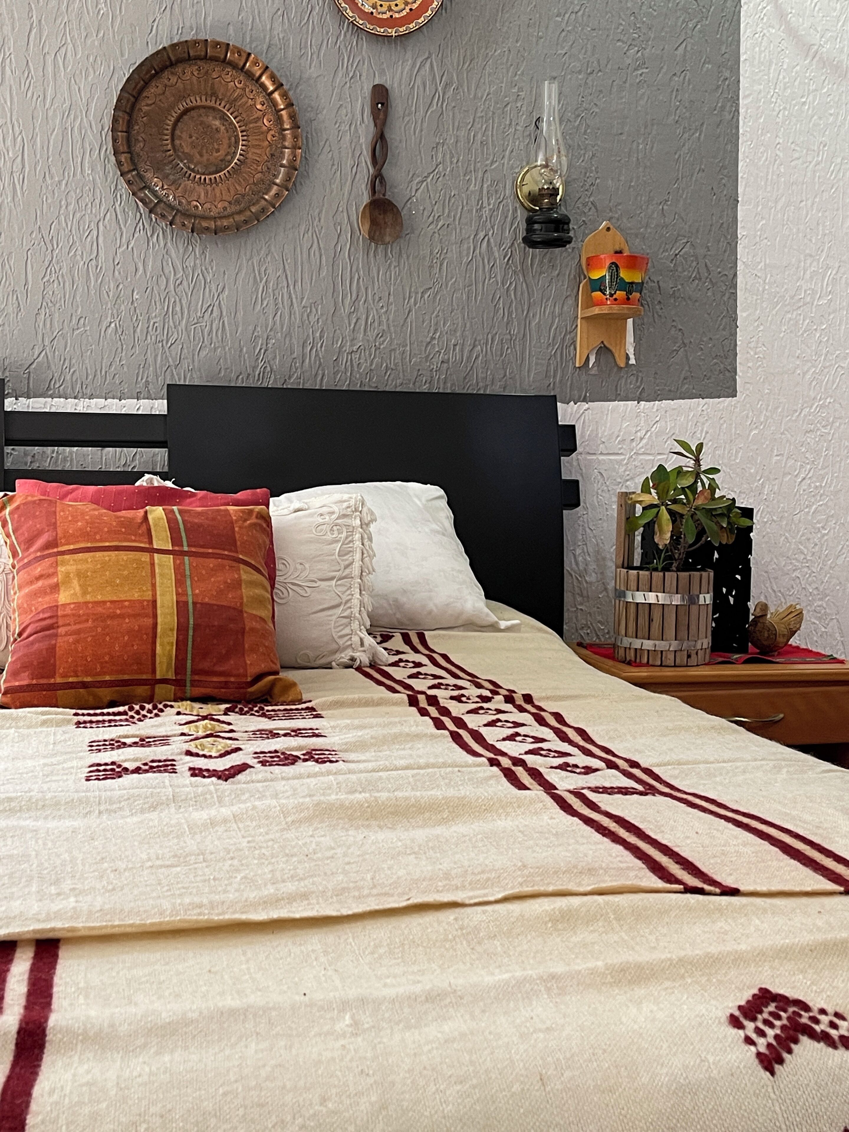 A bedroom with a bed, pillows, a bedside table, a wall clock, and a wall-mounted shelf with decorative items.