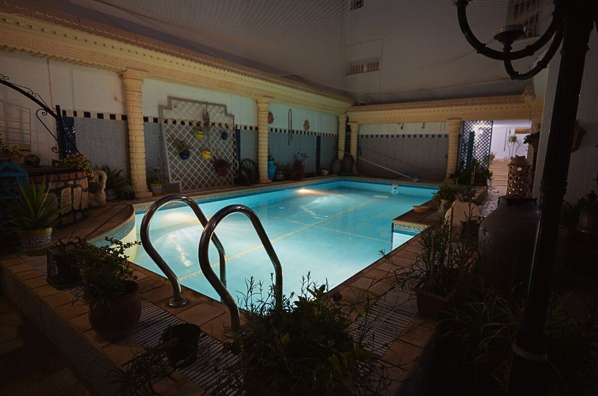 An indoor swimming pool with a tiled floor, surrounded by potted plants and a decorative railing.