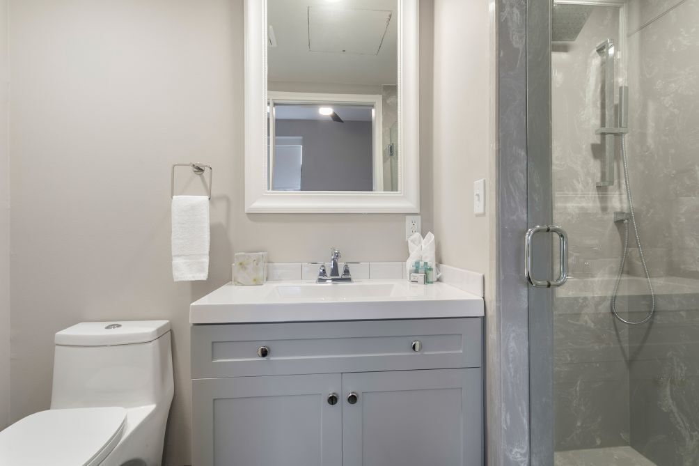 A bathroom with a toilet, sink, mirror, and shower.
