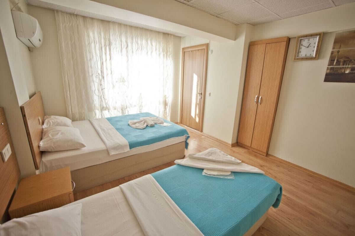 Habitación de hotel con dos camas, un armario de madera, un reloj en la pared y una ventana con cortinas.