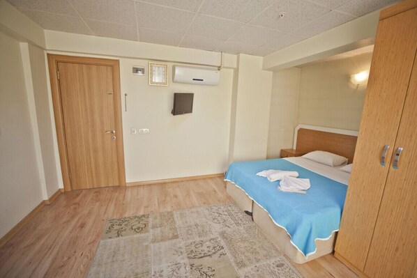 Un dormitorio con puerta de madera, aire acondicionado de pared, cama con colcha azul y armario de madera.