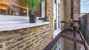 A brick building with a window sill, a potted plant, a metal bird sculpture, and a metal grill. - Prime Liverpool Street Retreat (London)