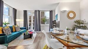A modern living room with a sofa, dining table, and a view through large windows. - Prime Liverpool Street Retreat (London)