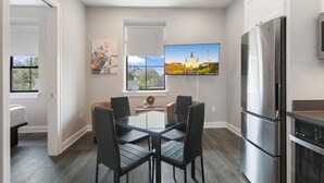 A modern kitchen with a large refrigerator, a dining table with chairs, and a flat-screen TV mounted on the wall. - Stylish 2BR Suite in Historic NOLA (New Orleans)