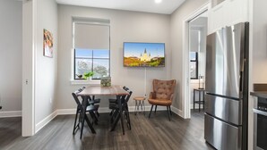 A modern kitchen with a dining table, chairs, a large refrigerator, and a window with a cityscape view.