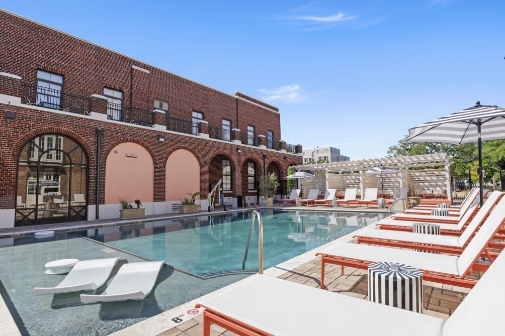A pool area with lounge chairs and a brick building in the background.