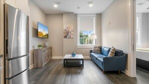 Eine moderne Küche mit einem Edelstahl-Kühlschrank, Holzschränken, einem dunklen Couchtisch und einem blauen Sofa.