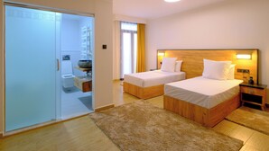 A hotel room with two single beds, a wooden headboard, a bedside table, a nightstand, a bathroom with a toilet and sink, and a sliding door closet. - hotel baba aroudj  (Jijel)