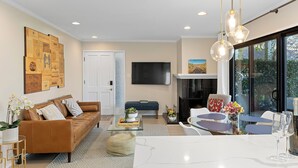 Un salon moderne avec un canapé en cuir marron, une table basse en verre, un téléviseur à écran plat et un coin repas comprenant une table et des chaises en verre.