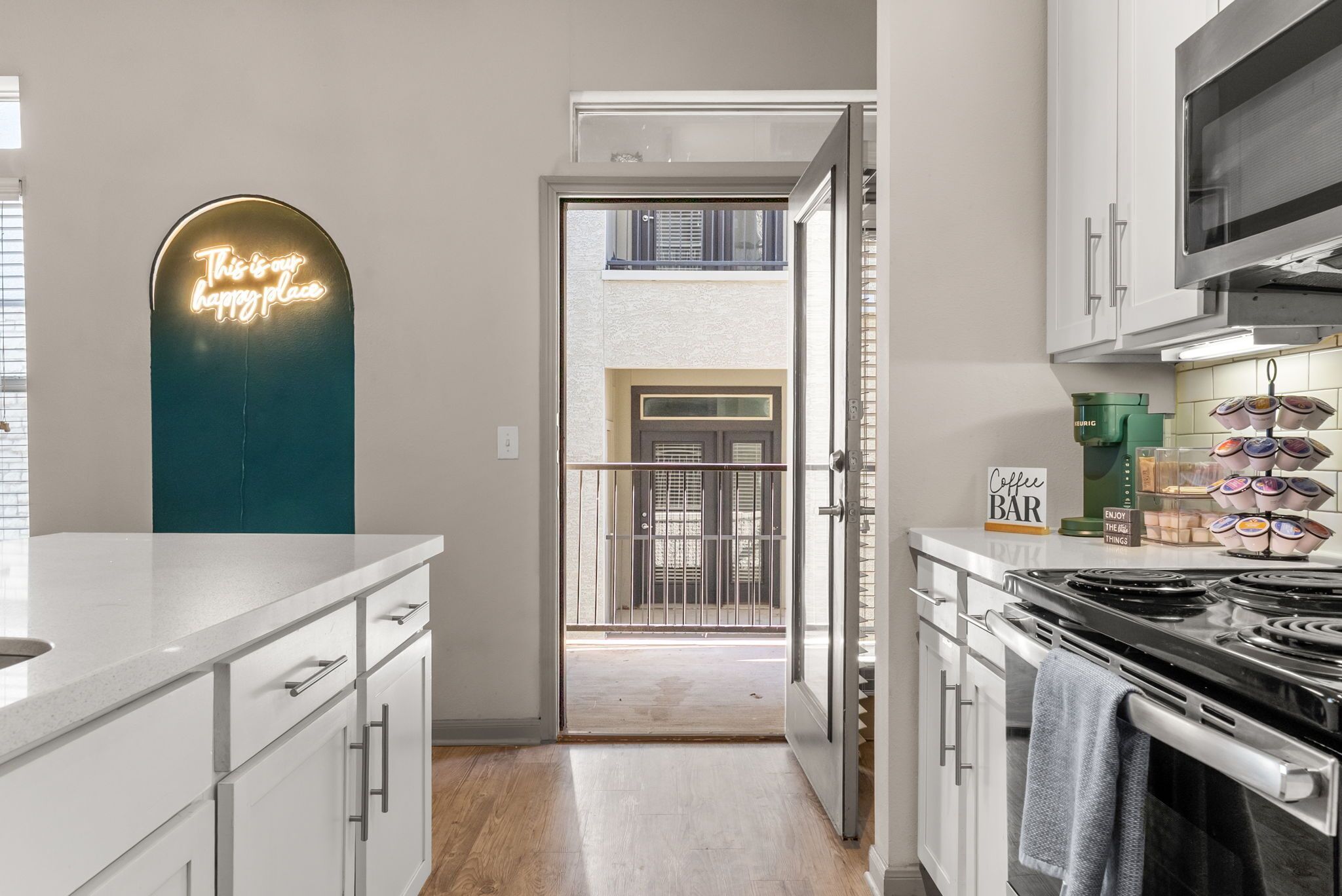 A modern kitchen with white cabinetry, a neon sign, and a view to a balcony.