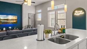 Cozinha moderna com uma ilha grande, ventilador de teto, luminárias pendentes, um letreiro neon e vista para o exterior.