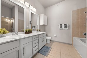 Un baño moderno con dos lavamanos, un espejo grande, un inodoro y una bañera.