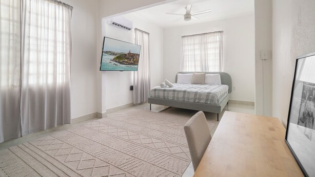 A bedroom with a bed, a desk, a chair, a ceiling fan, and a TV mounted on the wall. - San Juan Home DownTown Perfect for family and group (San Juan)