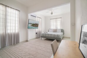 Un dormitorio con cama, escritorio, silla, ventilador de techo y televisor montado en la pared.