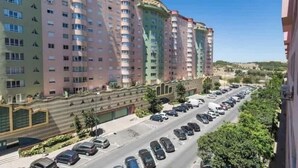 A multi-story building with a curved facade, a parking lot with cars, and a clear sky. - Fantastic apartment with lots of light, in a quiet area, 200m from the metro. (Lisboa)