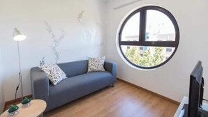 A room with a grey sofa, a round window, a flat-screen TV, and a lamp. - Fantastic apartment with lots of light, in a quiet area, 200m from the metro. (Lisboa)