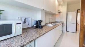 A modern kitchen with white cabinets, a granite countertop, a microwave, a coffee maker, and a refrigerator. - Fantastic apartment with lots of light, in a quiet area, 200m from the metro. (Lisboa)