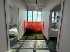 A narrow hallway with a window at the end, leading to a room with a bed and a small table.