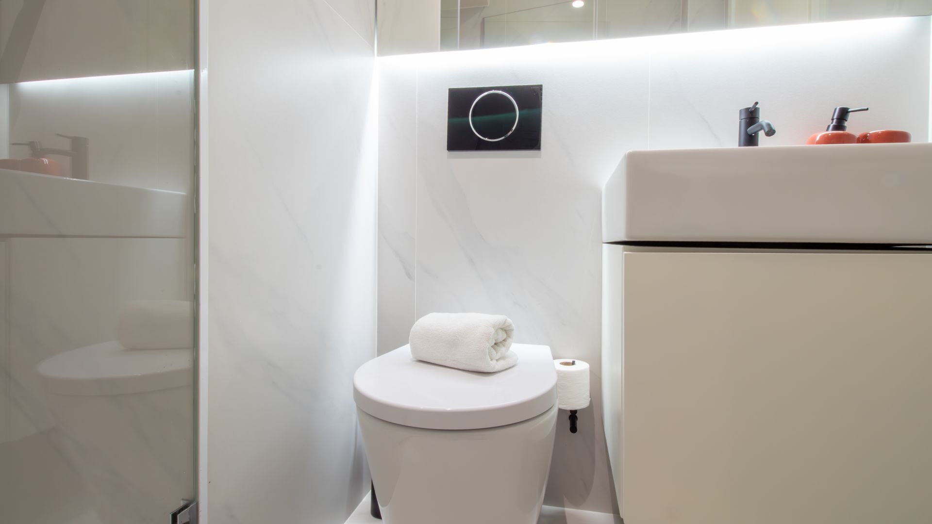Ein modernes Badezimmer mit Toilette, Handtuch und Waschbecken mit Seifenspendern.