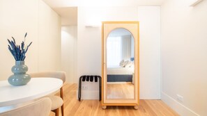 A modern bedroom with a large mirror, a bed with pillows, a small table with a vase, and a trash bin. - Miguel Bombarda House - 301 by LovelyStay (Porto)