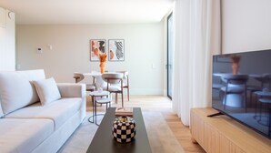 En moderne stue med sofa, sofabord med dekorativ vase, fladskærms-tv og spiseplads med stole og bord.