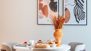 A dining table with breakfast items, a vase with dried plants, and abstract art on the wall. - Miguel Bombarda House - 302 by LovelyStay (Porto)