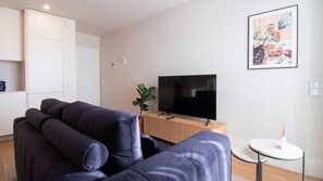 Ein modernes Wohnzimmer mit einem dunkelblauen Sofa, einem Flachbildfernseher auf einem Holzboden, einem kleinen runden Tisch und einem Blumentopf.