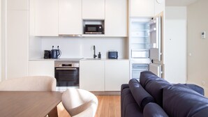 A compact kitchen with a microwave, toaster, and oven. There is a sofa and a dining table in the living area. - Miguel Bombarda House - 402 by LovelyStay (Porto)