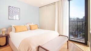 A bedroom with a large bed, a bedside table with a lamp, a framed picture on the wall, and a view of the outside through a balcony. - Miguel Bombarda House - 402 by LovelyStay (Porto)