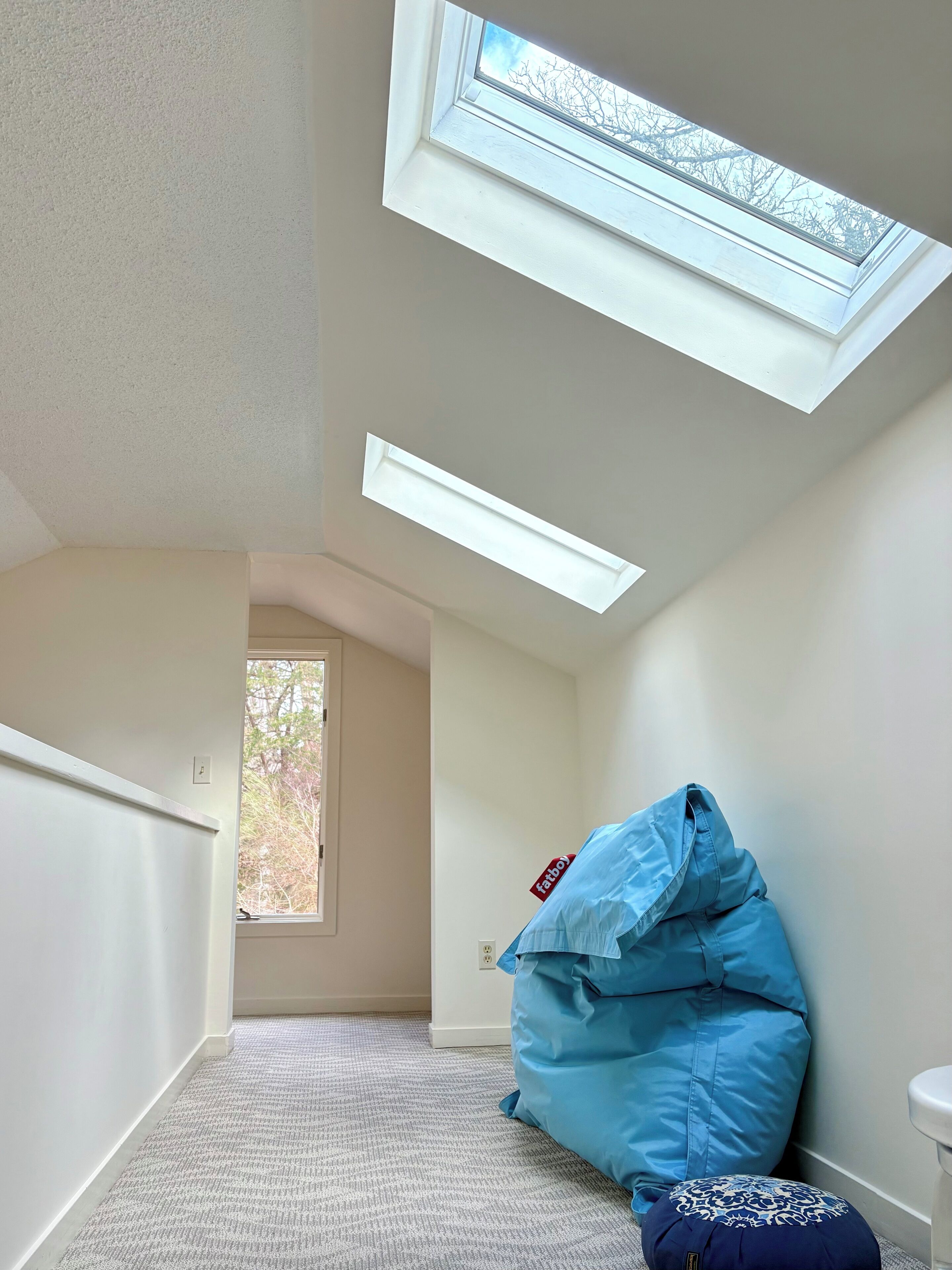 A room with a skylight, a blue bean bag, and a patterned ottoman.
