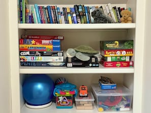 Een boekenplank met verschillende boeken, spelletjes en speelgoed.