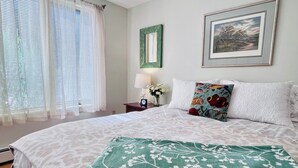 A neatly arranged bedroom with a large bed, a bedside table with a lamp, and a framed picture on the wall.