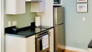A modern kitchen with white cabinets, stainless steel appliances, and a wooden floor.