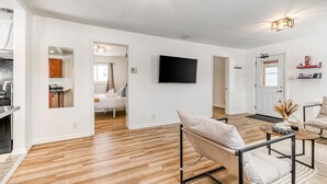 A modern living room with a wooden floor, a sofa, a coffee table, and a TV mounted on the wall. - Charming 2 Bed, 1 Bath Escape | Free Parking, WiFi (Greater Sudbury)