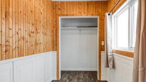 A room with wooden panel walls, a white closet, and a window with curtains. - Charming 2 Bed, 1 Bath Escape | Free Parking, WiFi (Greater Sudbury)