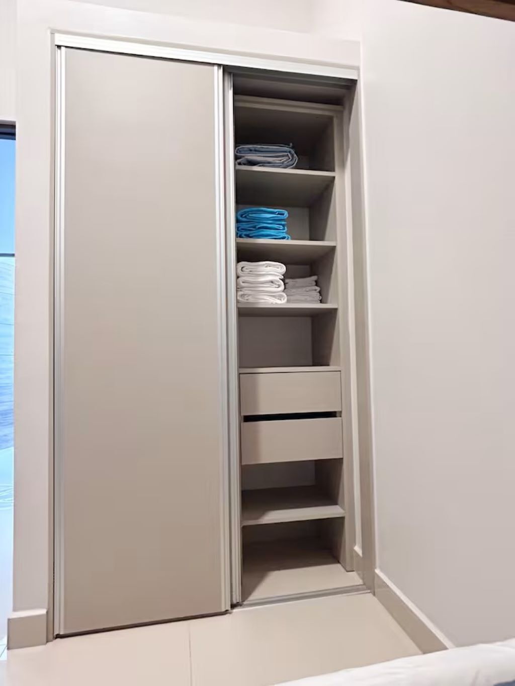 Een inloopkast met planken en lades, gevuld met opgevouwen kleding.