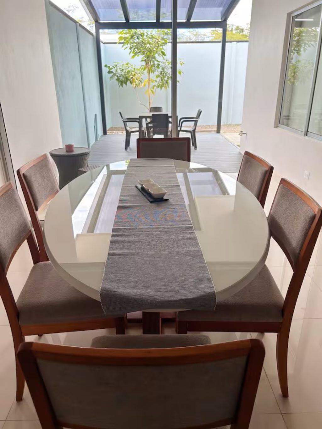 A dining area with a glass table, wooden chairs, and a view of the outdoors.