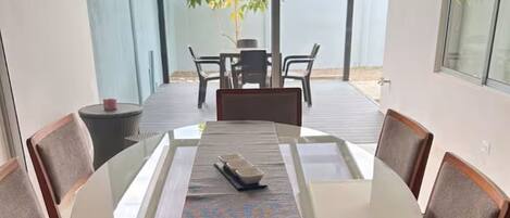A dining area with a glass table, wooden chairs, and a view of the outdoors.